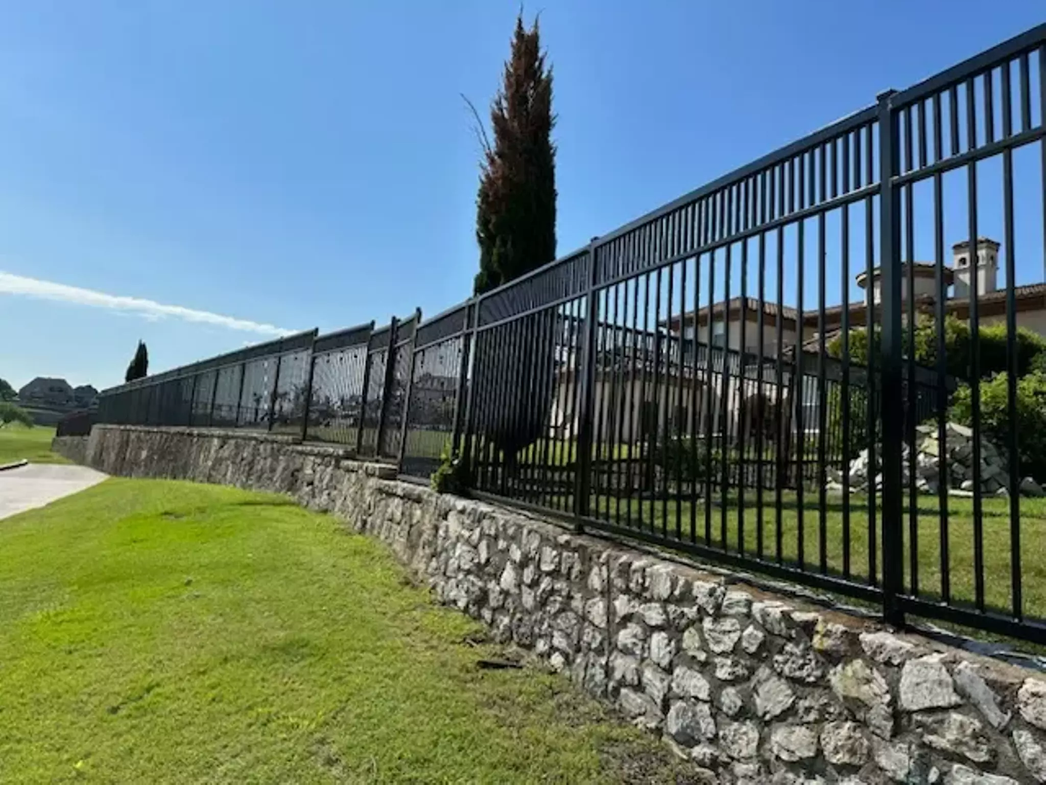 Black wrought iron fence atop a stone wall with greenery