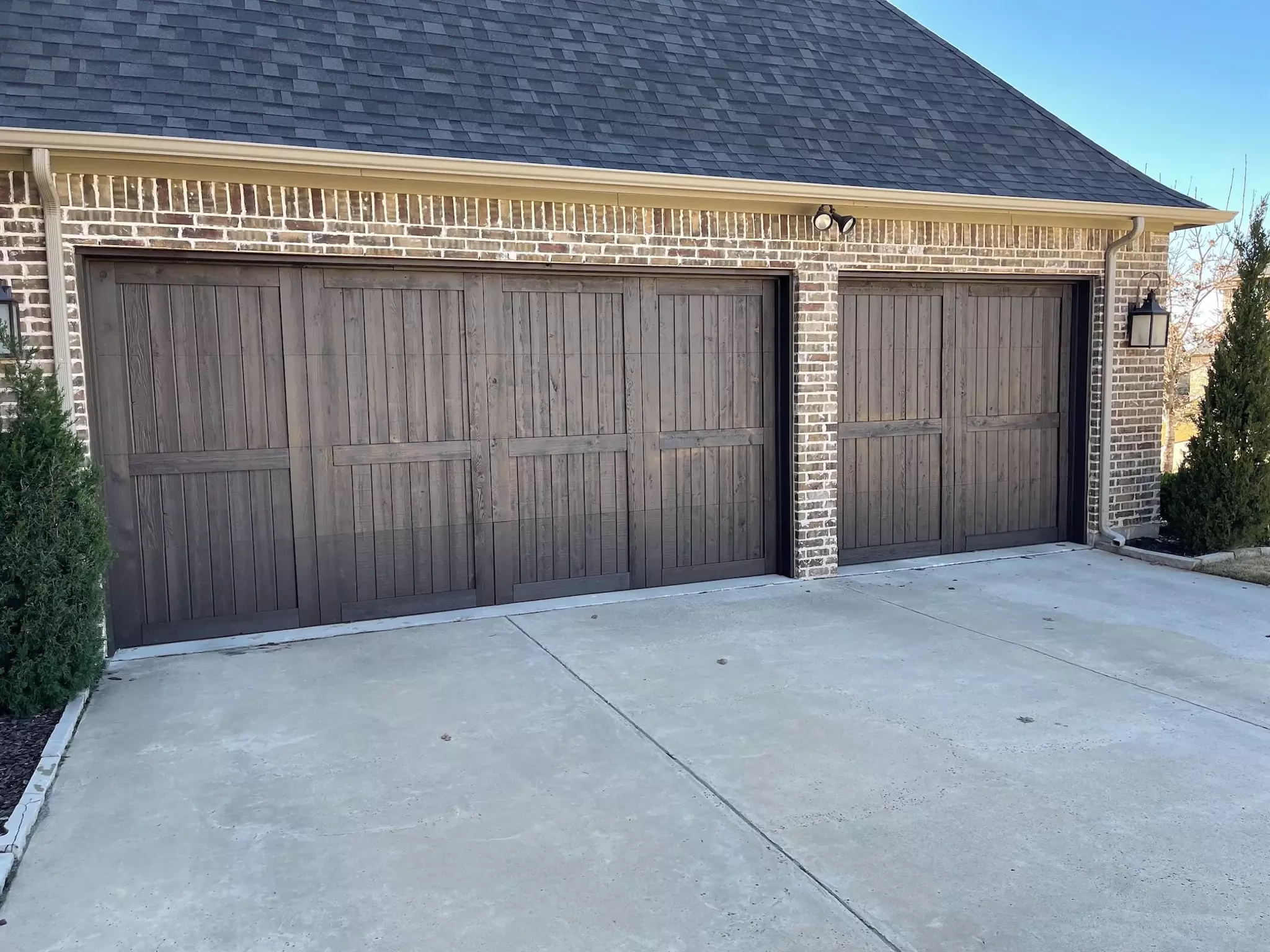 Dark gray stained wooden garage door on brick house