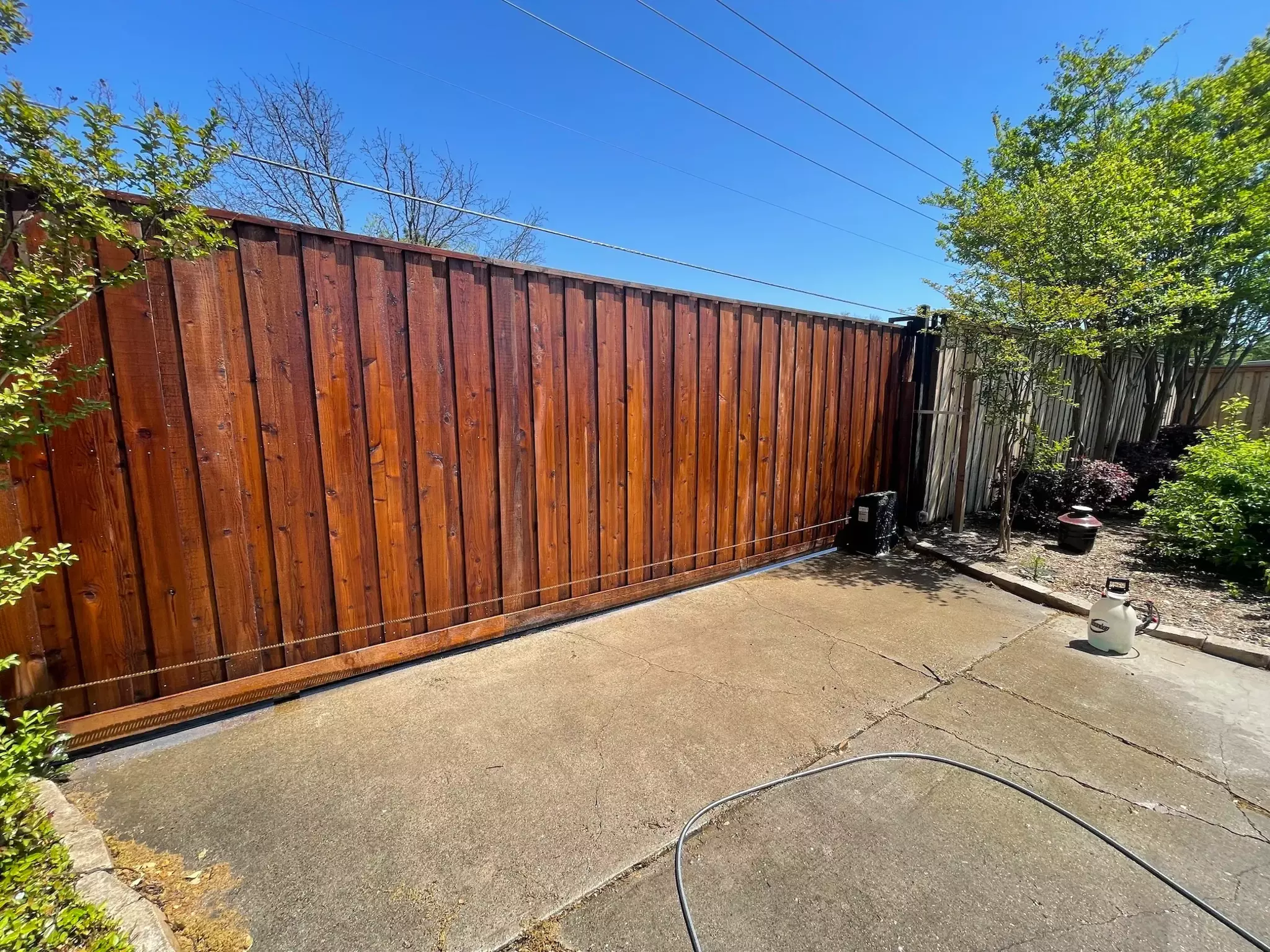 Deep brown stained wooden automatic gate along a brown wooden fence on a driveway