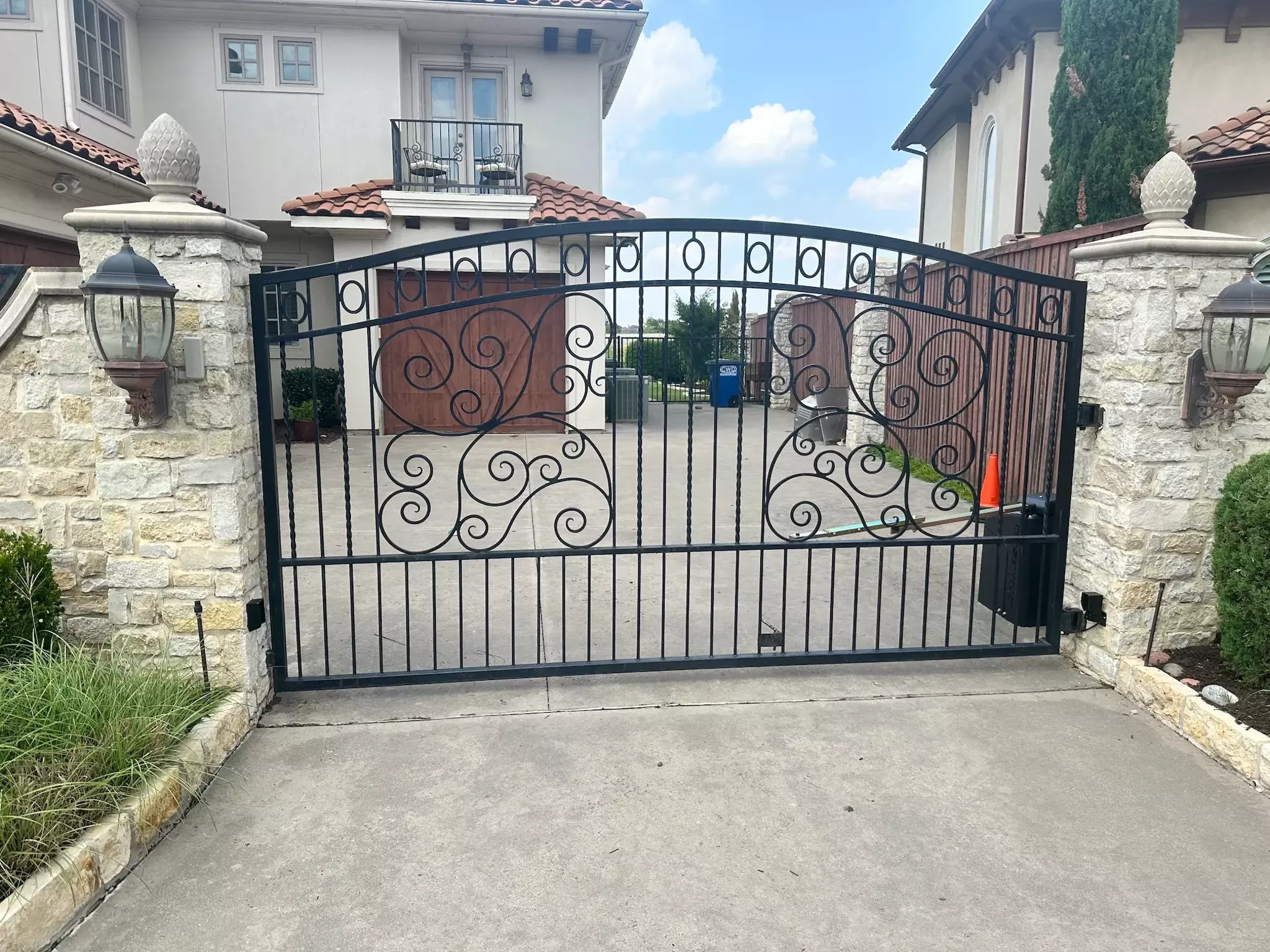 Black wrought iron automatic gate with elegant design attached to stone walls