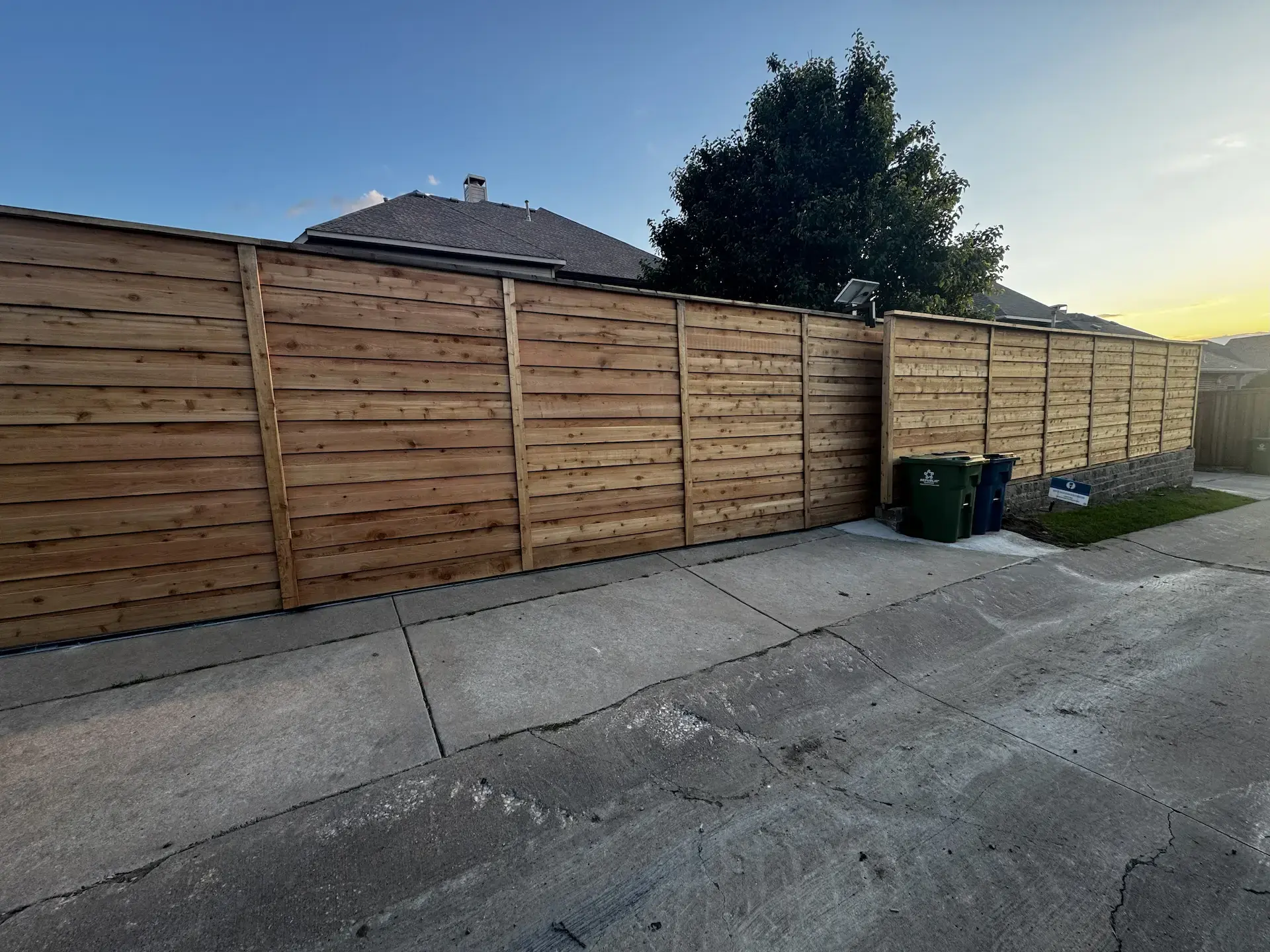 Unstained wooden fence in a residential backyard from the sidewalk