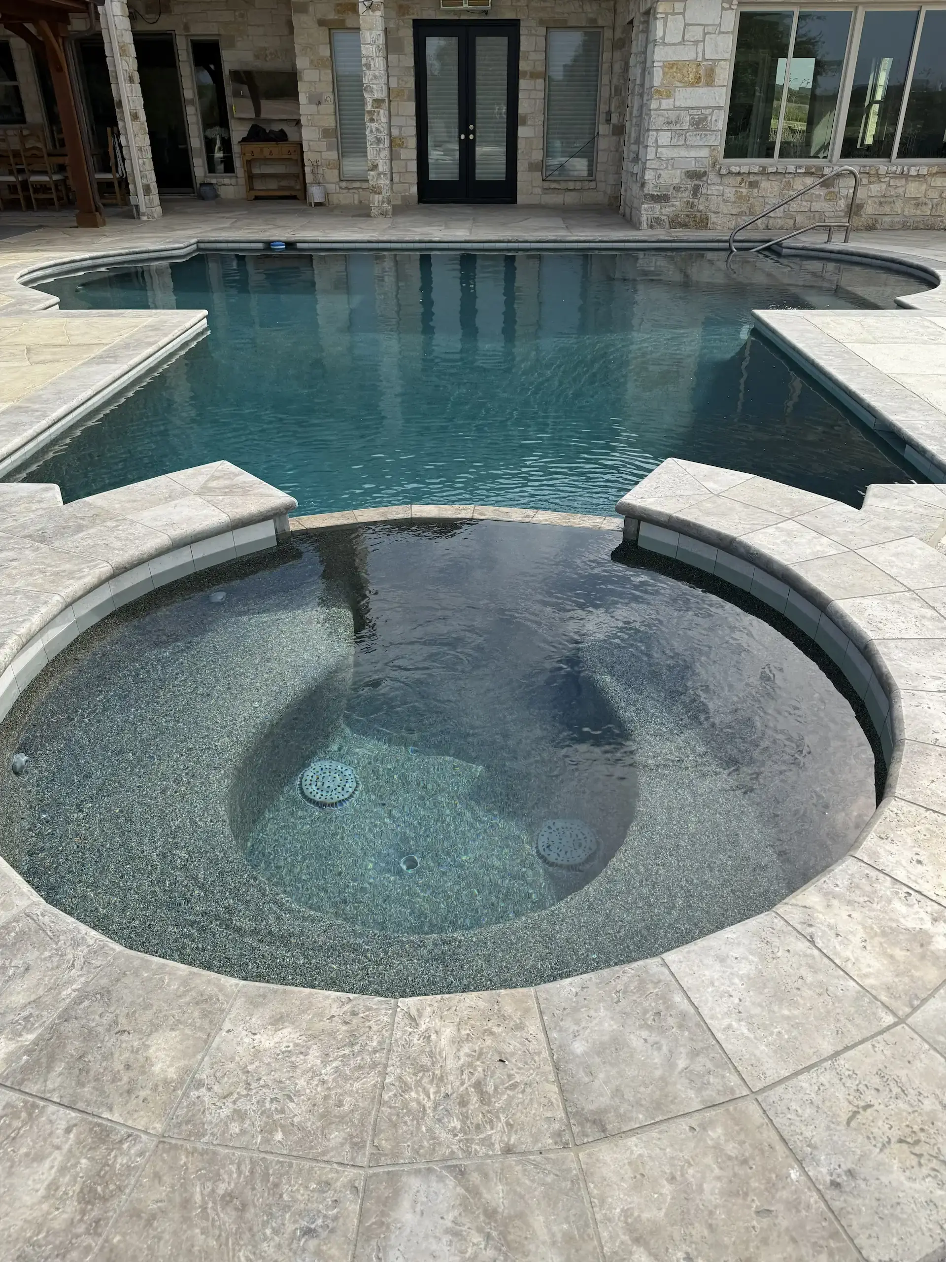 Circular inset hot tub next to a larger pool set in concrete taken from just above looking down